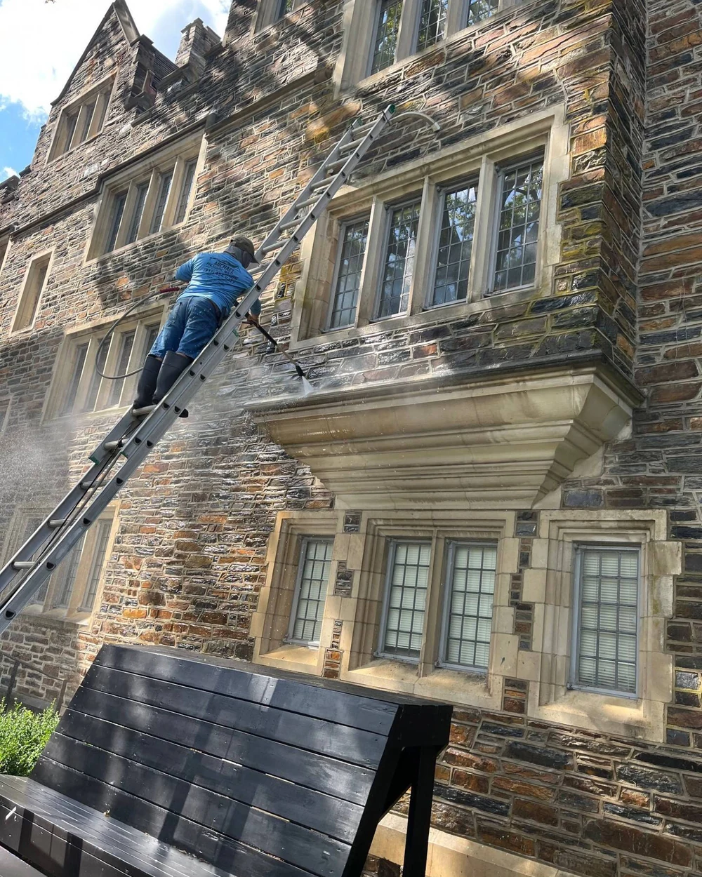 Durham Power Wash worker cleaning the exterior of a multistory stone building