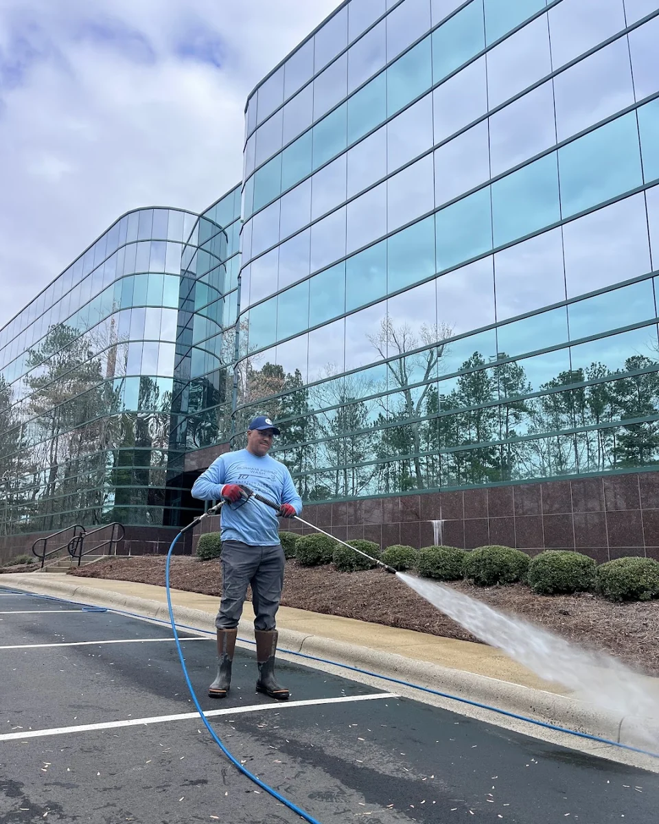 Worker pressure washing a concrete curb beside a glass commercial building