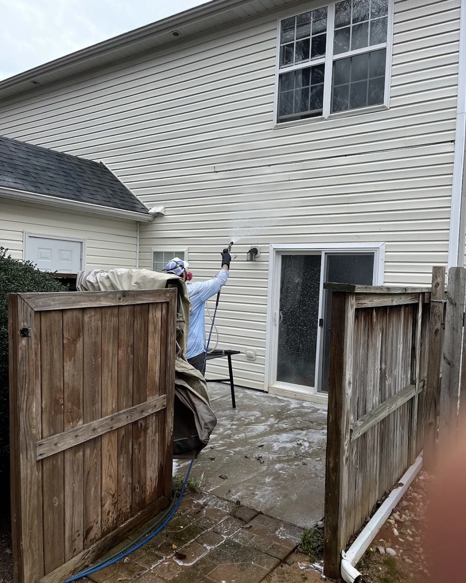 Worker washing the siding of a white two-story home