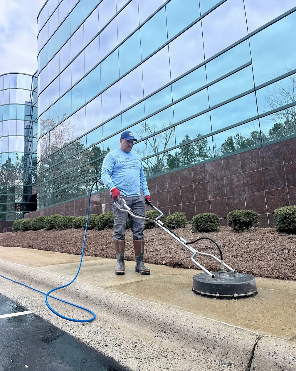 Worker using a circular surface cleaner on a commercial sidewalk